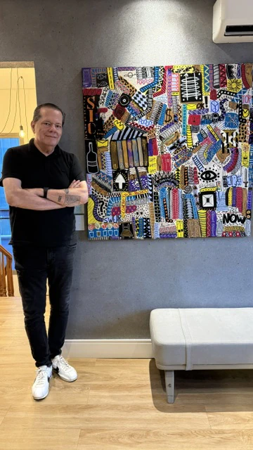 Alessandro standing beside a colorful painting installed in an exhibition room.