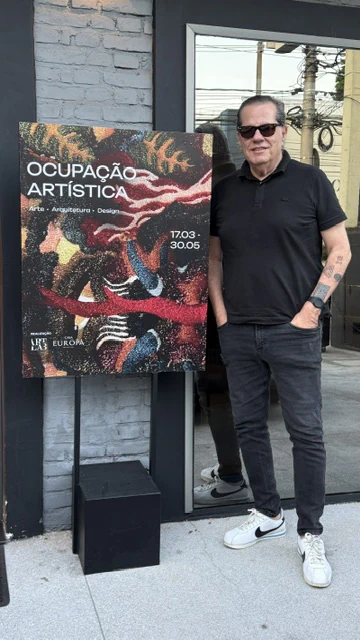 Alessandro beside an Occupação Artística exhibition poster.