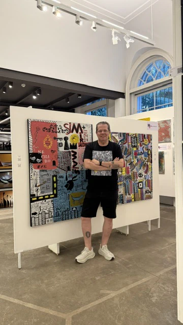 Alessandro with two large paintings displayed in an exhibition hall.