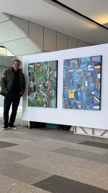 Alessandro beside two paintings installed on an exhibition panel.