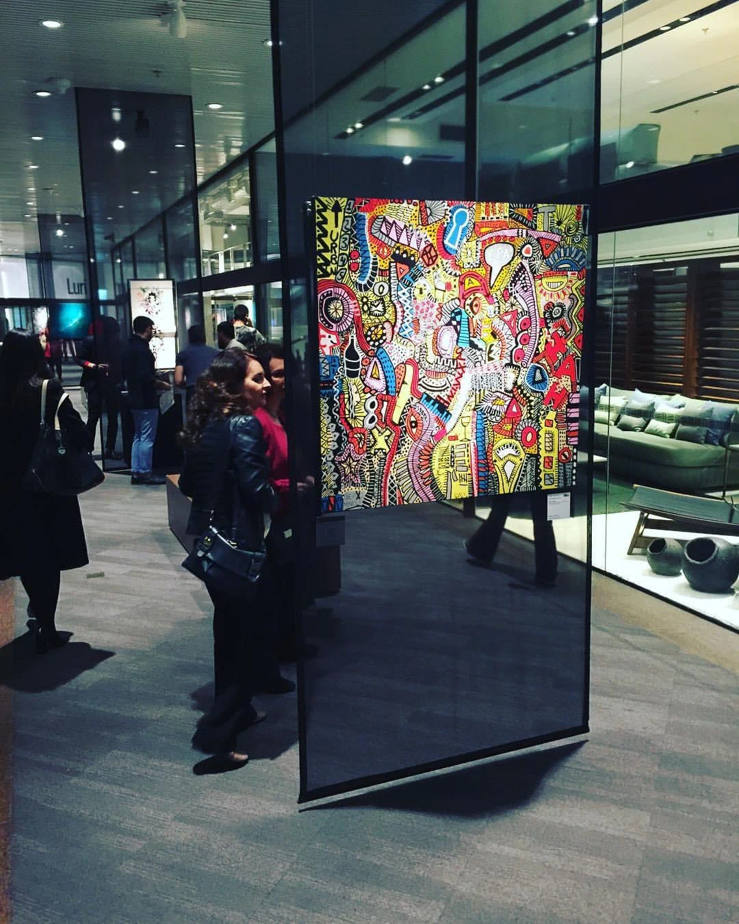 A large Alessandro painting on a freestanding panel during a public exhibition.