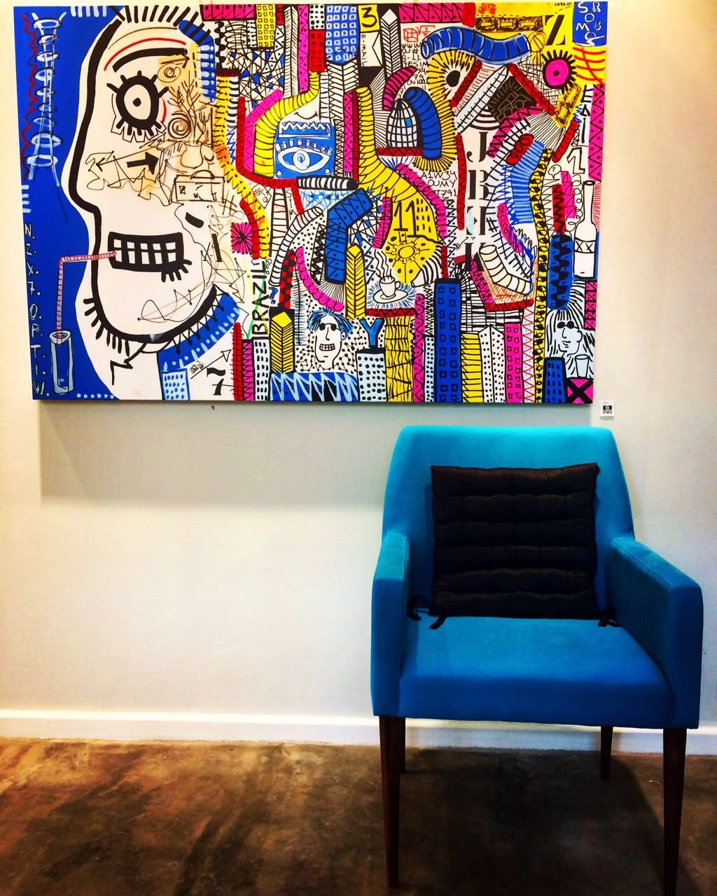 A colorful Alessandro painting displayed above a blue armchair.