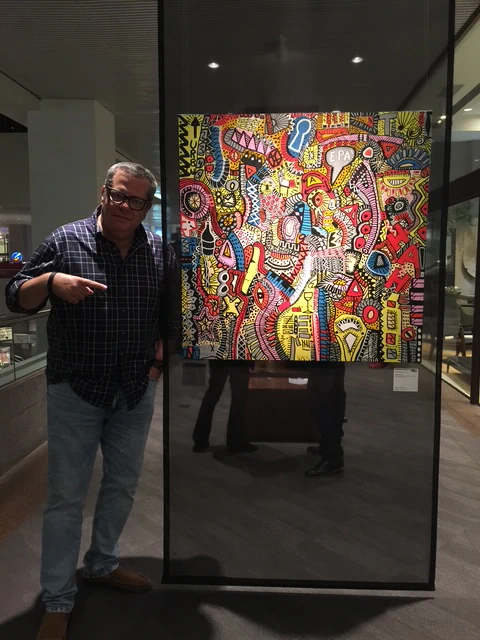 Alessandro beside a painting mounted on a freestanding exhibition panel.